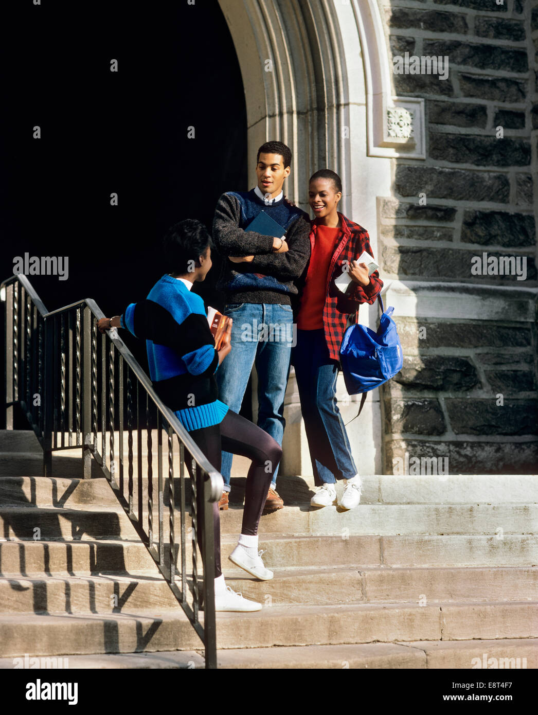 1980s THREE AFRICAN AMERICAN STUDENTS MEETING AND TALKING ON SCHOOL STEPS Stock Photo