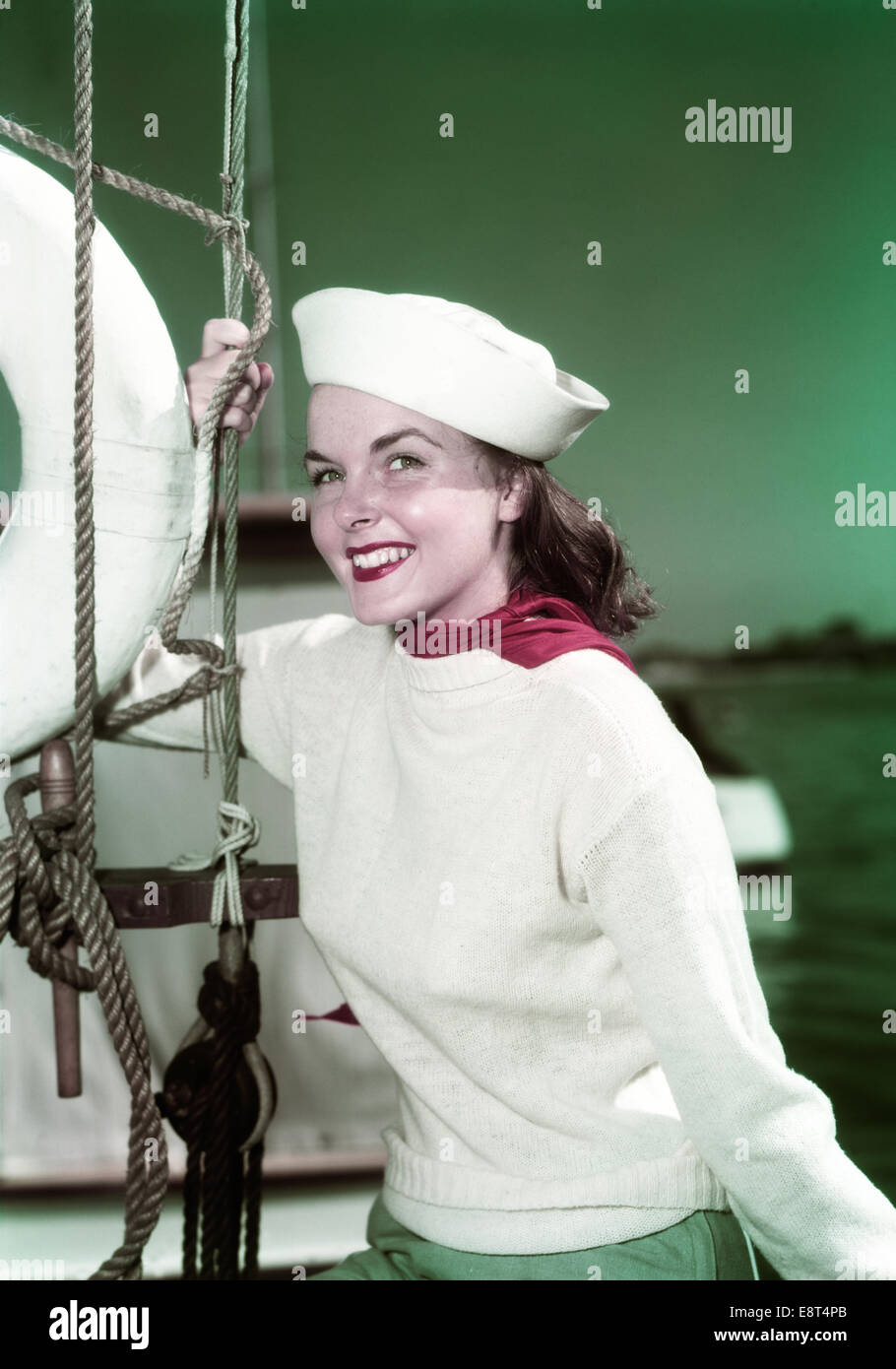 1940s PORTRAIT SMILING WOMAN WEARING SAILOR HAT YACHTING OUTFIT POSING BY SAILBOAT RIGGING LOOKING AT CAMERA Stock Photo