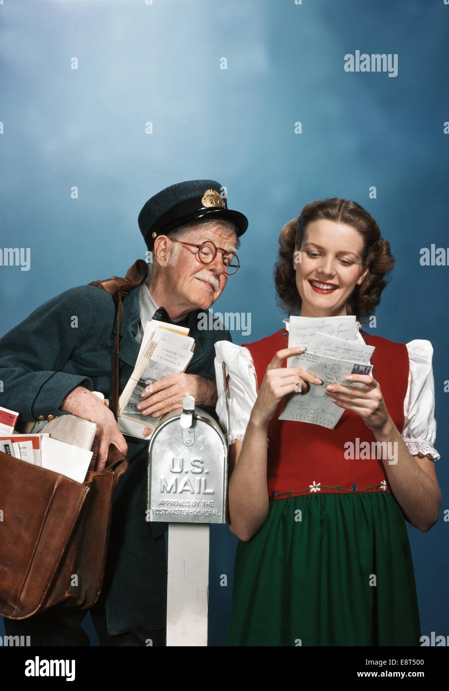 1940s SMILING WOMAN READING LETTERS LEANING ON MAILBOX ELDERLY SENIOR MAILMAN READING OVER SHOULDER Stock Photo