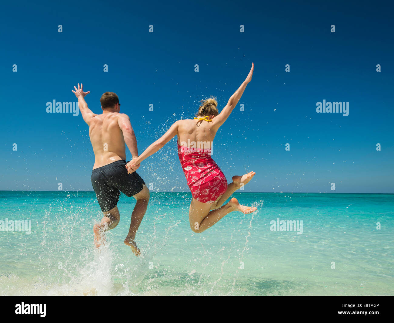 Caucasian couple jumping for joy in tropical ocean Stock Photo