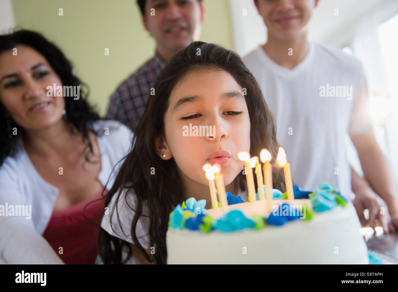 Hispanic girl blowing out candles on birthday cake Stock Photo