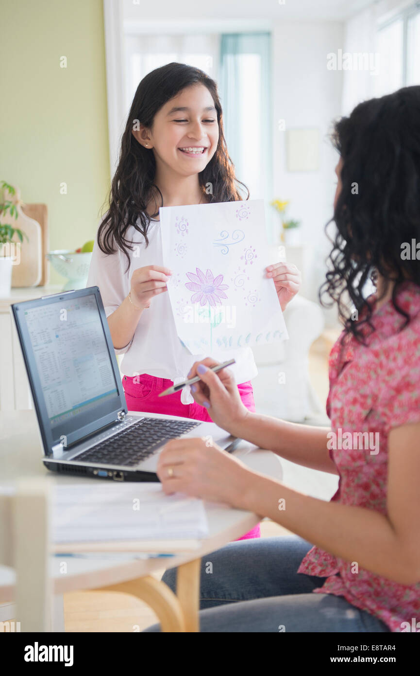 Hispanic girl proudly showing drawing to mother Stock Photo