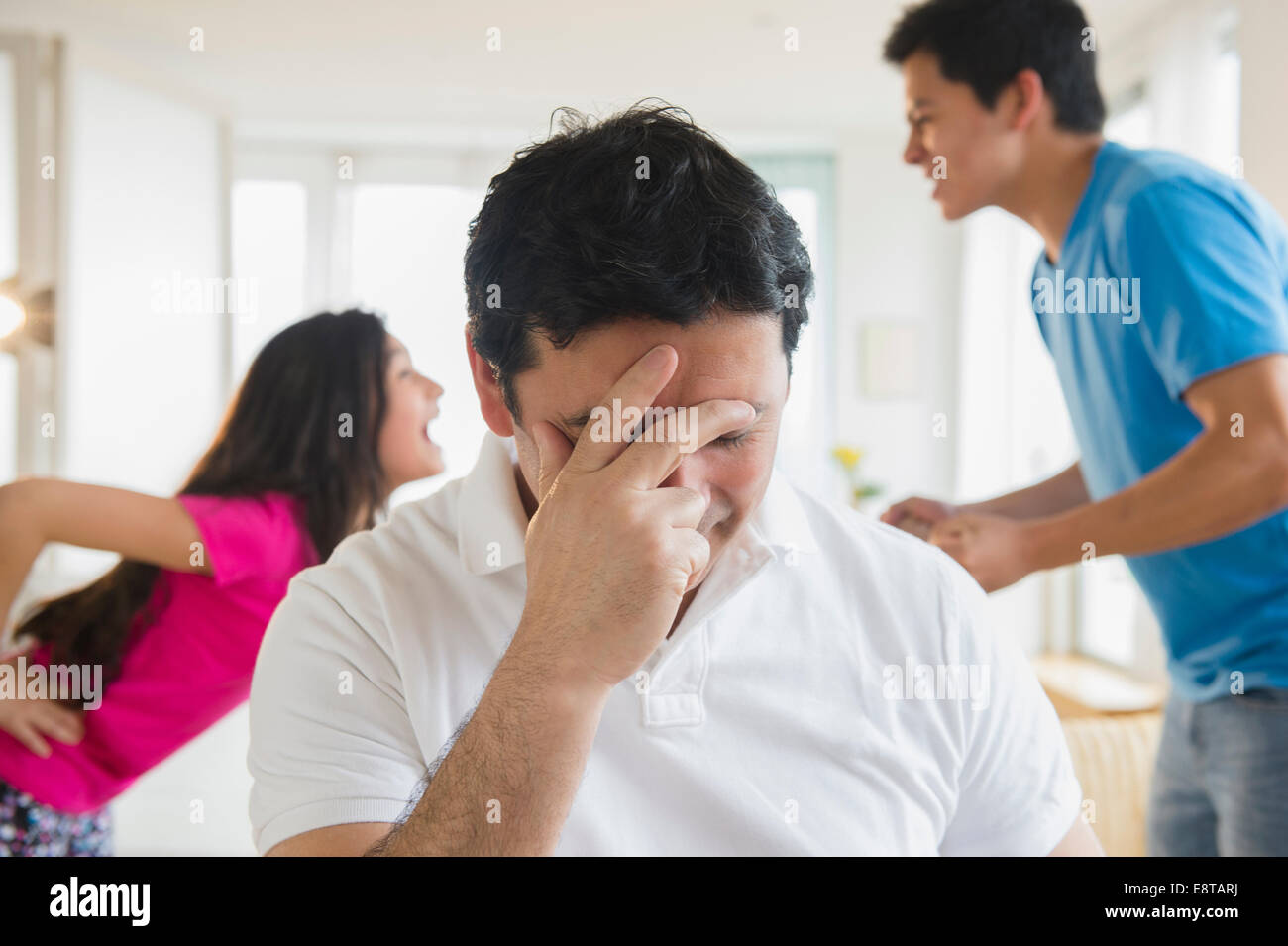 Hispanic father covering his face as children fight behind him Stock Photo