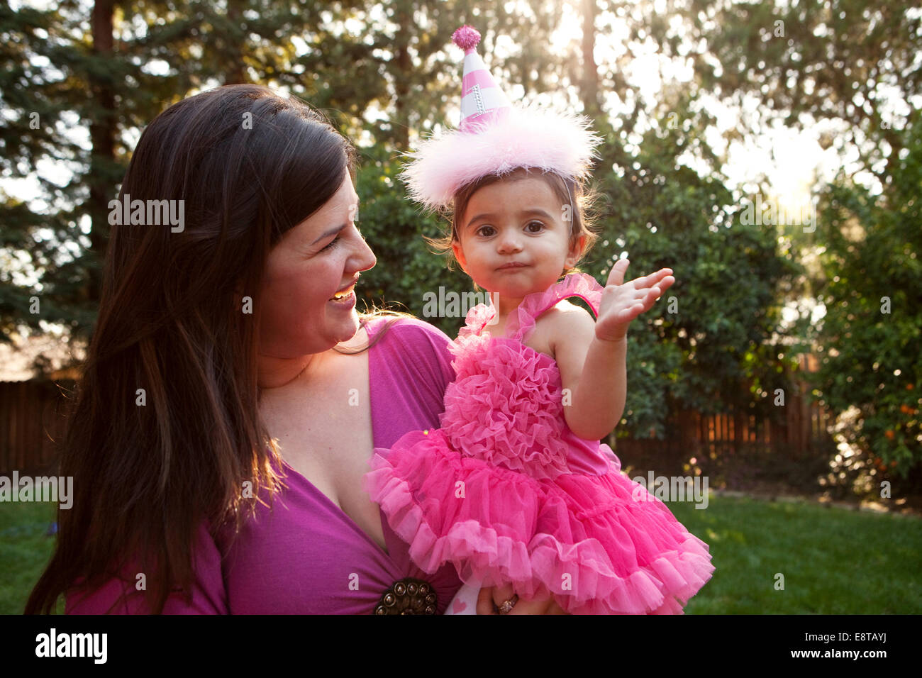 Mother holding daughter in party hat in backyard Stock Photo