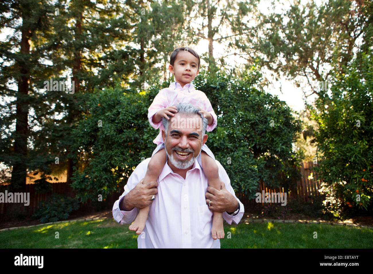 Grandfather carrying grandson on shoulders in backyard Stock Photo