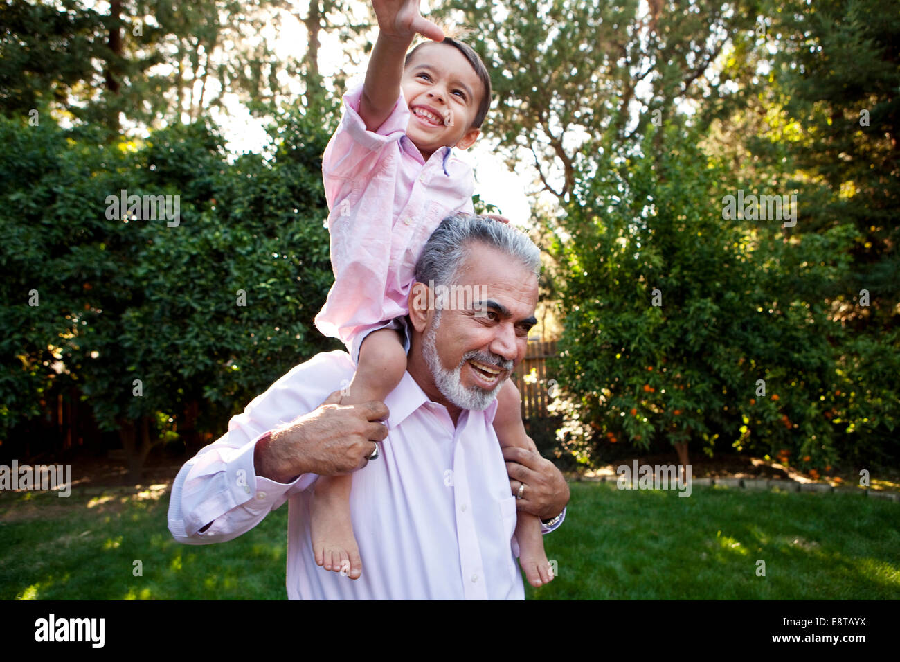 Grandfather carrying grandson on shoulders in backyard Stock Photo