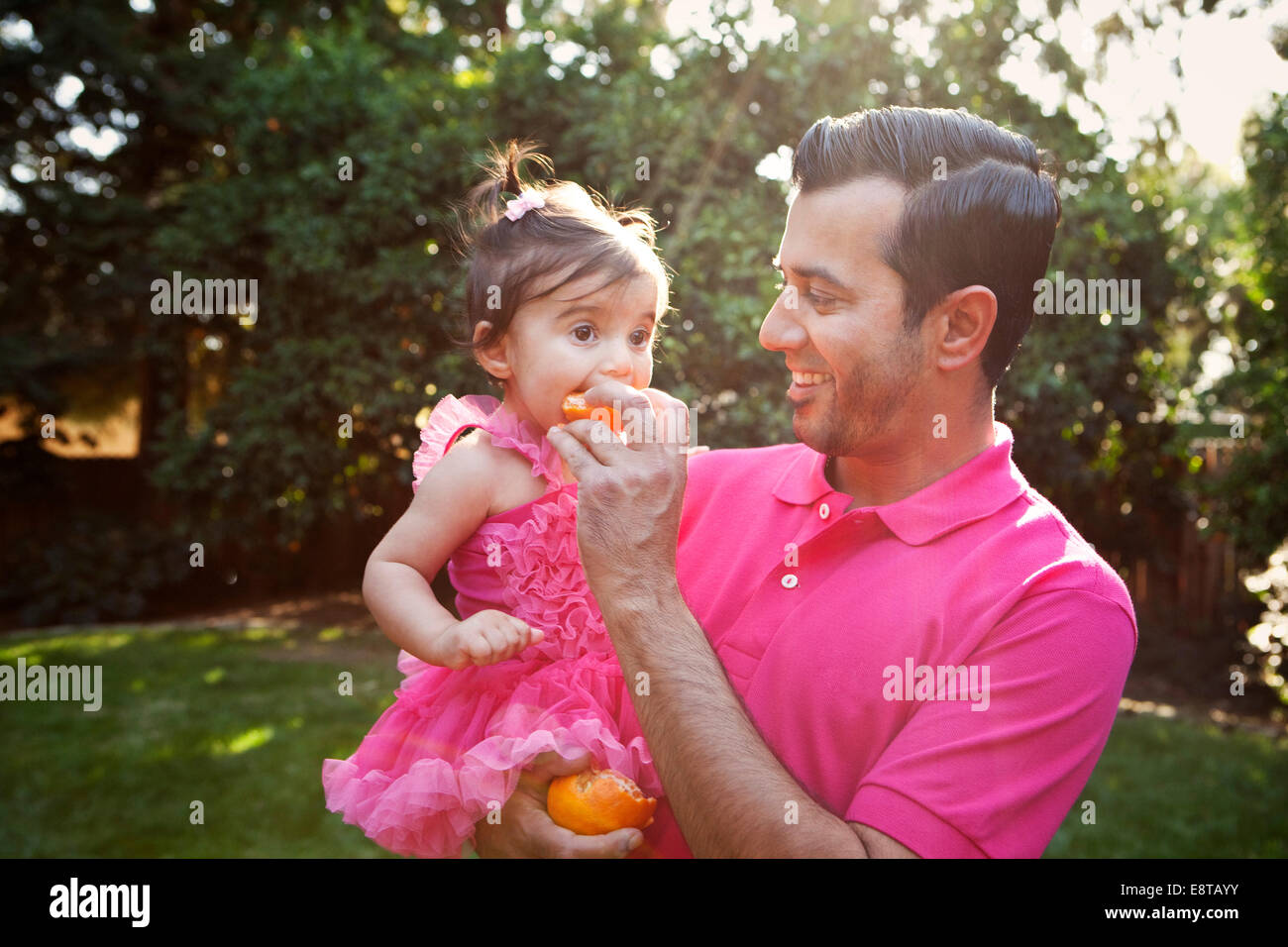 Father feeding daughter orange outdoors Stock Photo