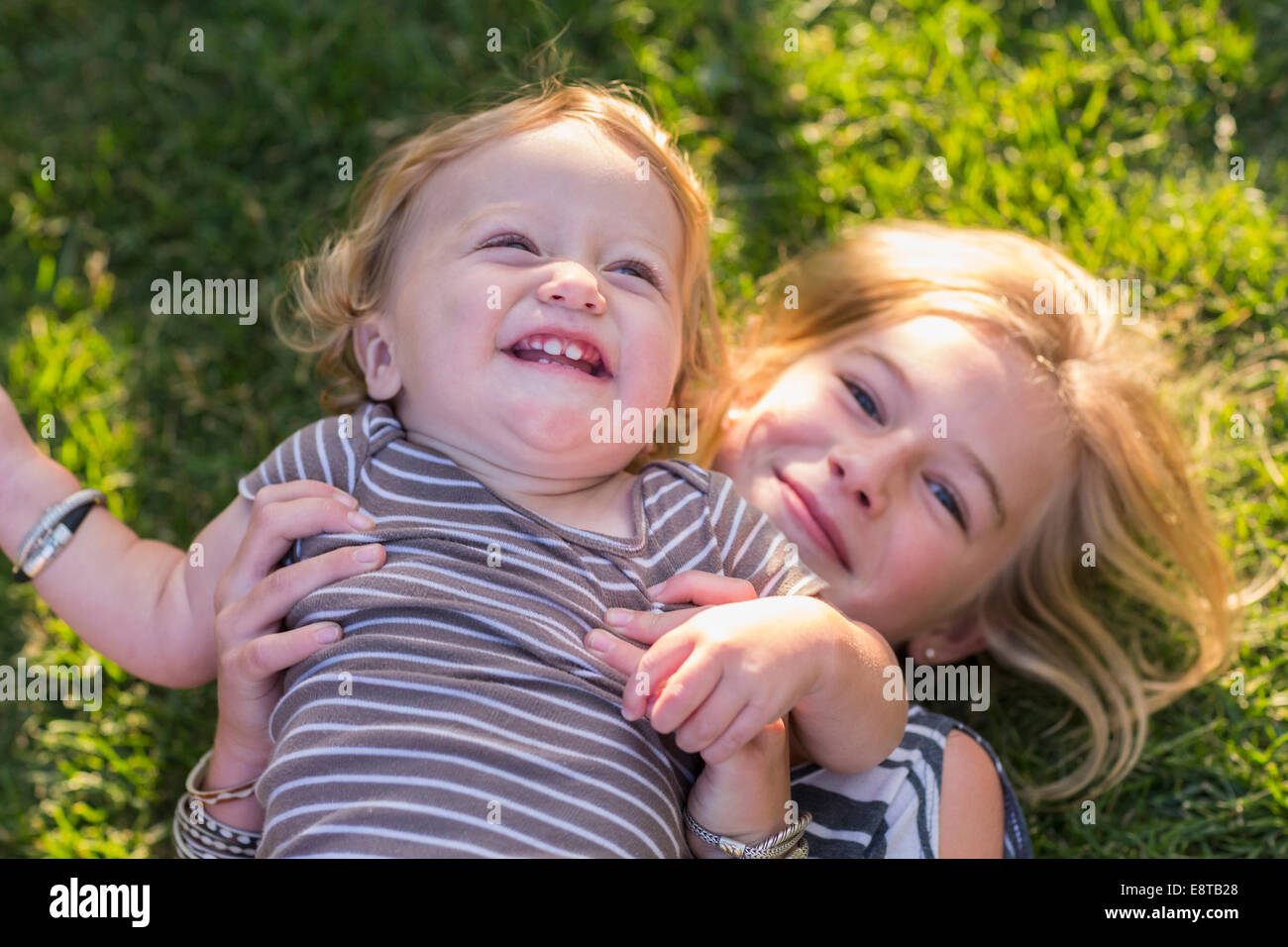 Caucasian sister holding baby brother in grass Stock Photo