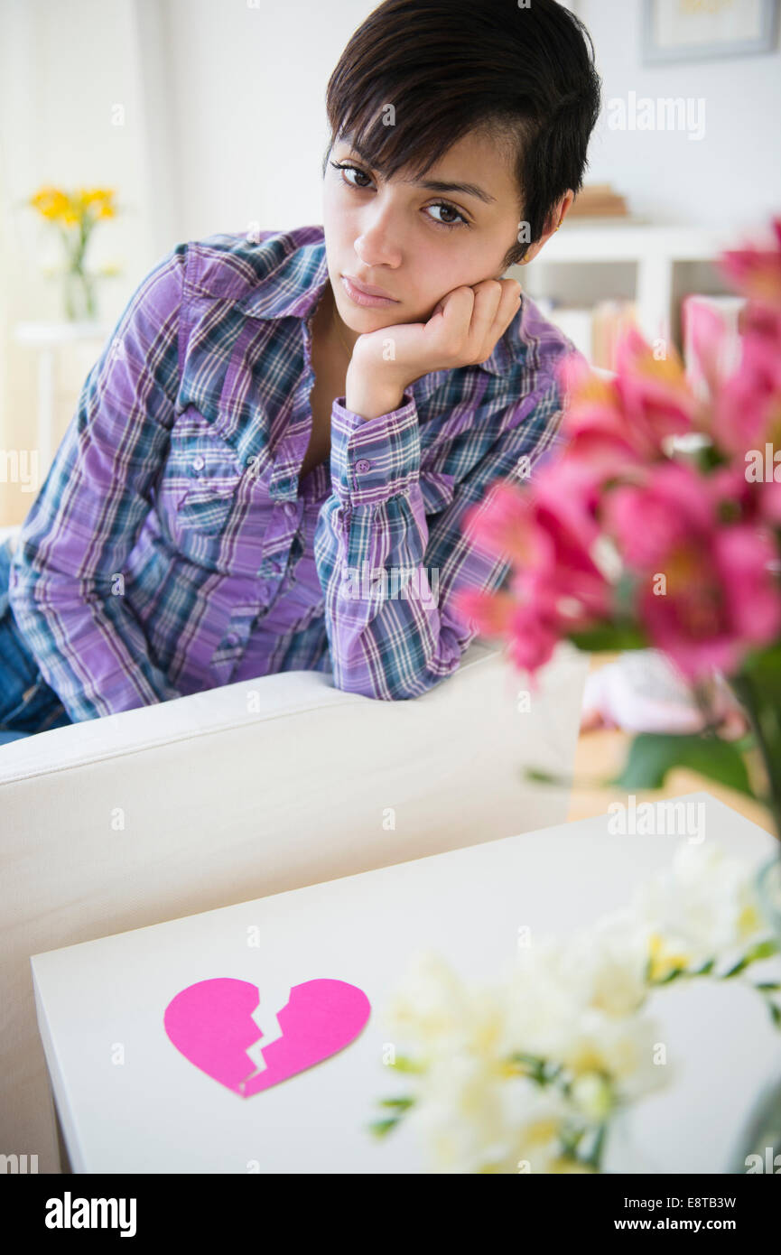 Sad mixed race woman on sofa with broken heart Stock Photo