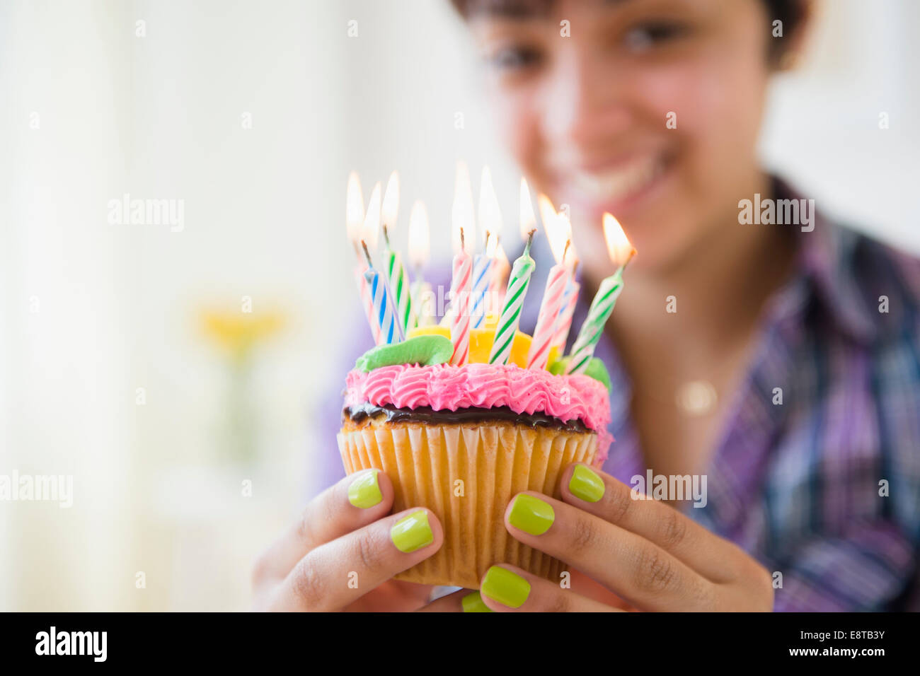Mixed race woman holding cupcake with birthday candles Stock Photo