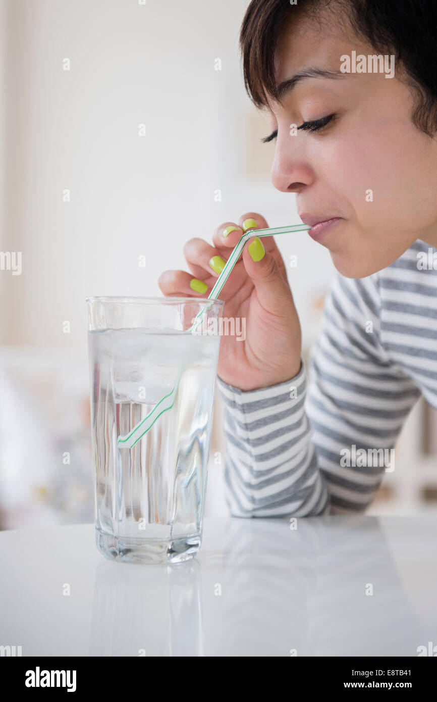 Mixed race woman drinking water with straw Stock Photo