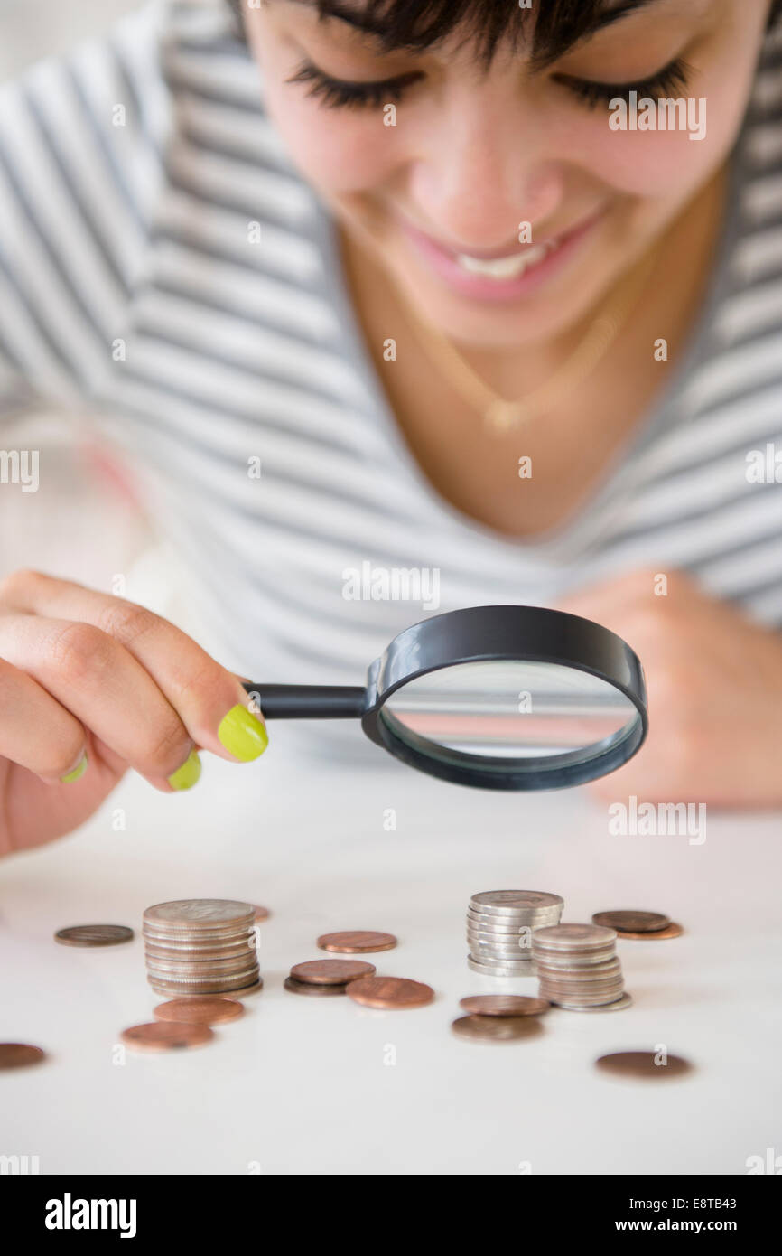 Mixed race woman examining stacks of coins with magnifying glass Stock Photo