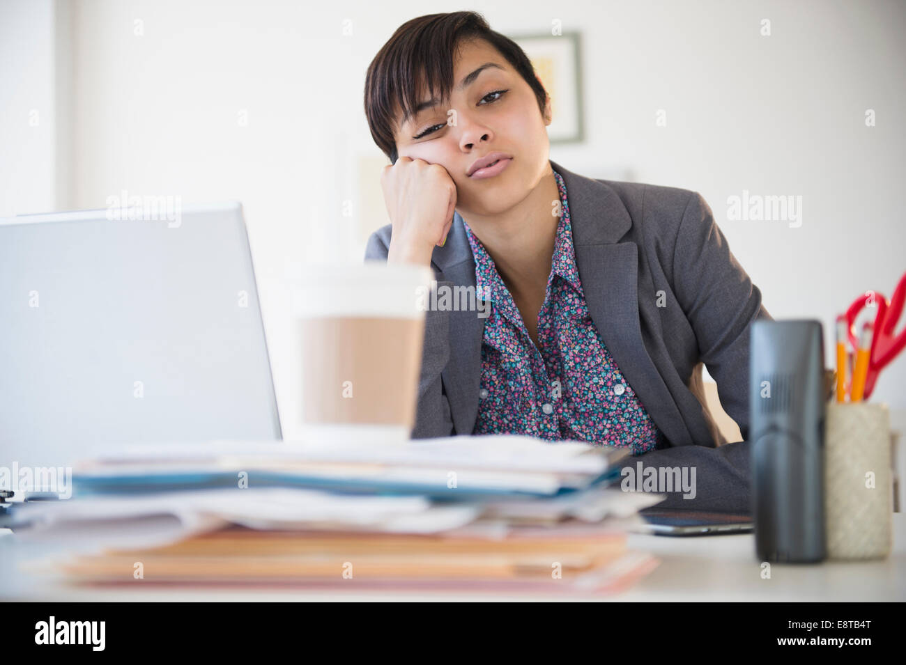 Bored mixed race businesswoman sitting at office desk Stock Photo
