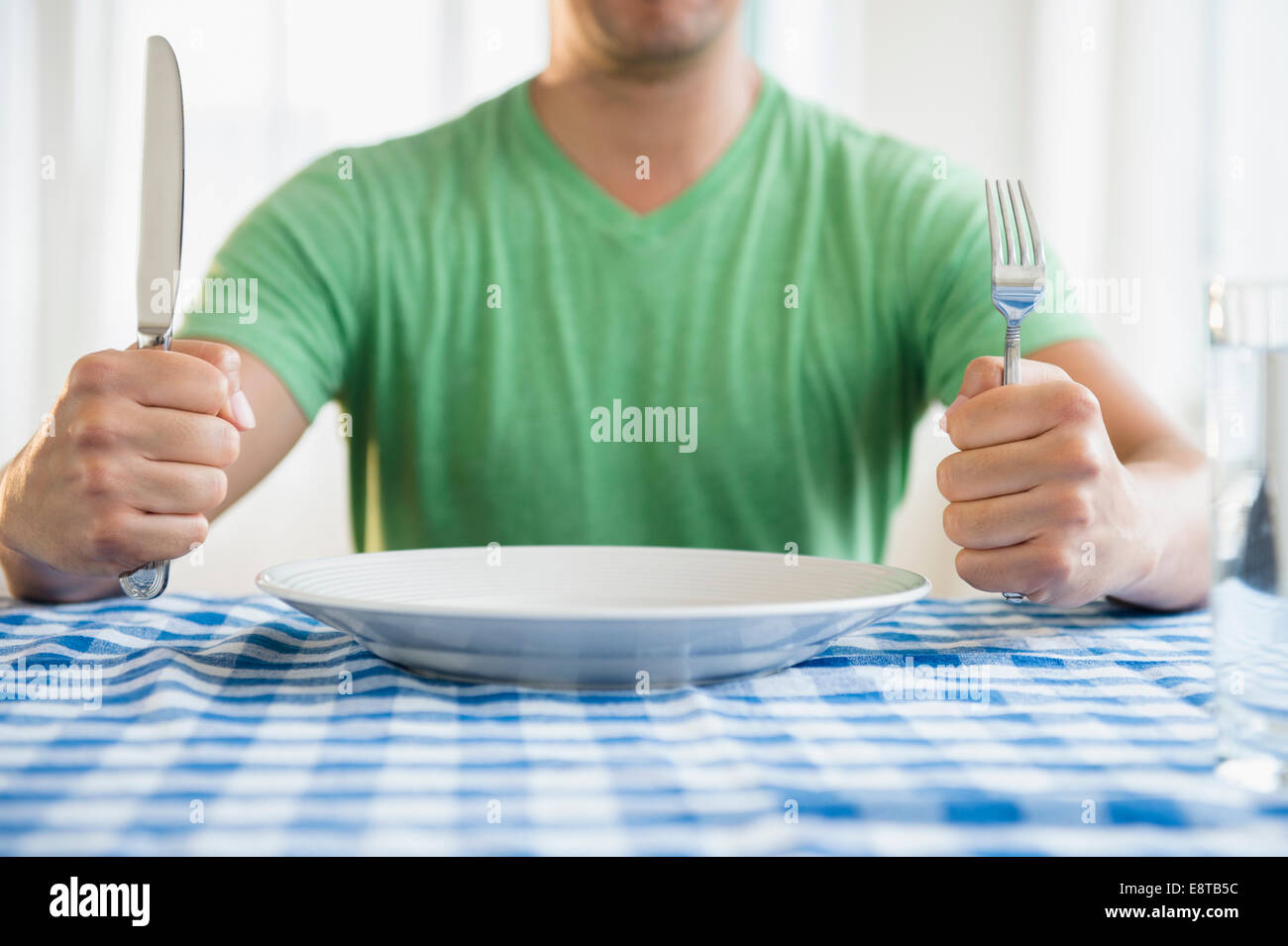 Mixed race man holding fork and knife at table Stock Photo - Alamy