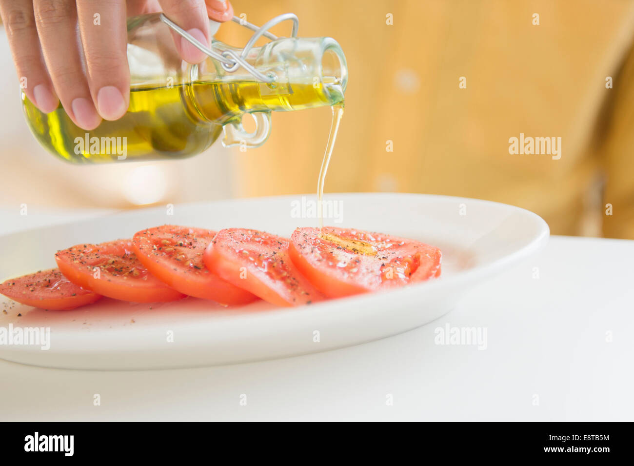 Close up of mixed race man pouring oil on tomatoes Stock Photo