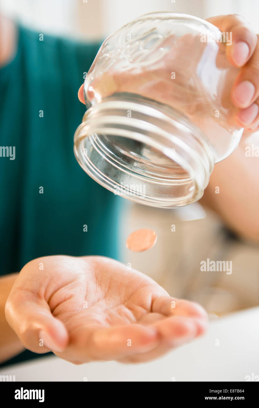 Close up of mixed race man pouring penny out of jar Stock Photo
