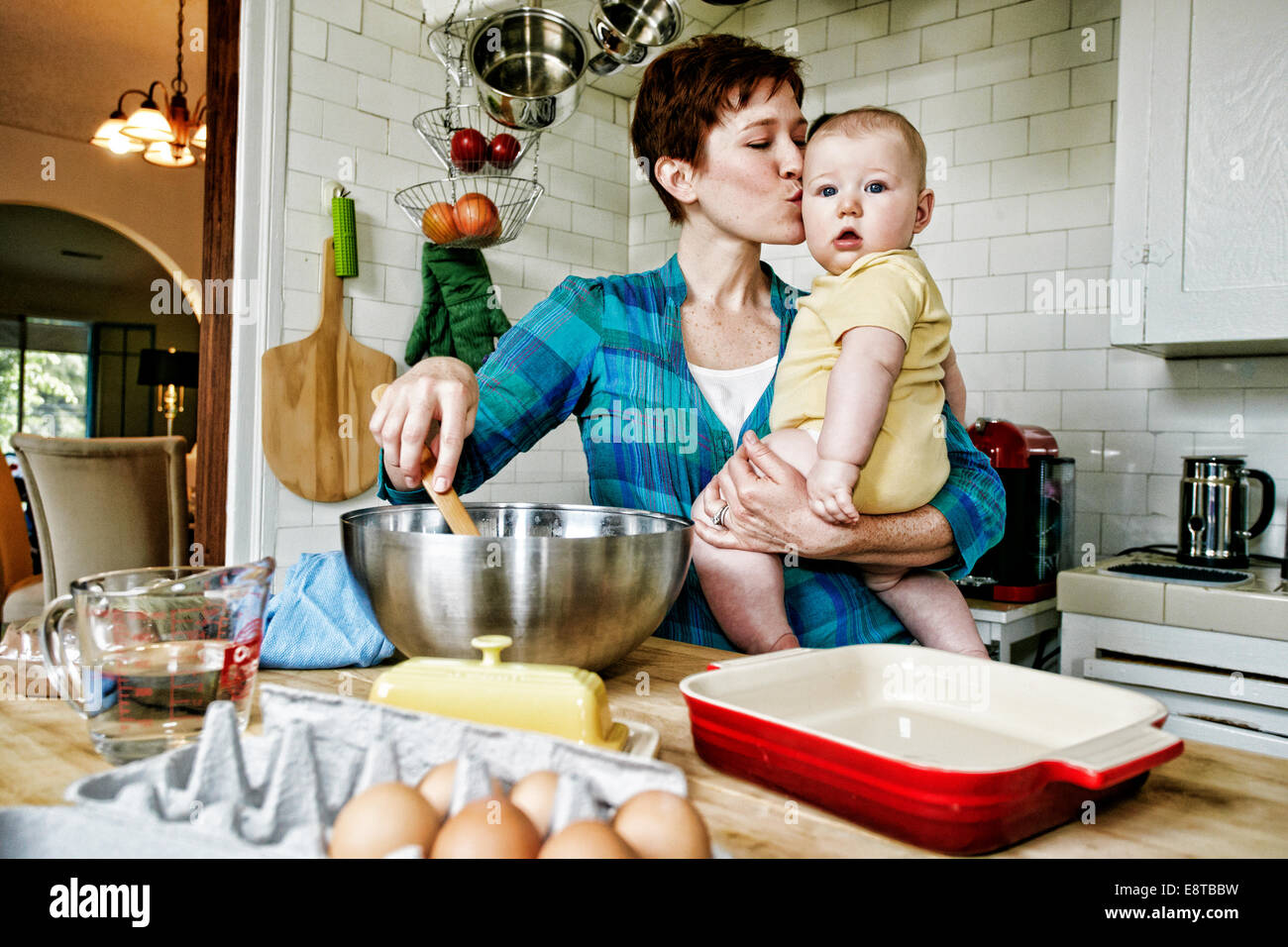 Caucasian mother kissing baby and cooking in kitchen Stock Photo