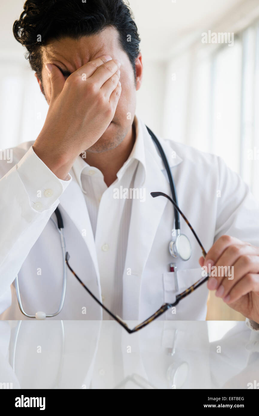 Close up of upset mixed race doctor rubbing his forehead Stock Photo