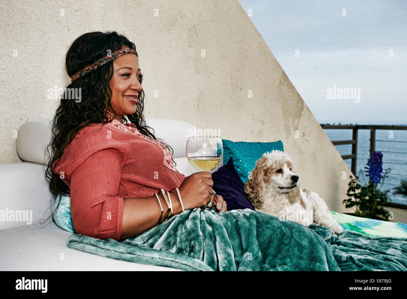 Mixed race woman drinking wine at waterfront with dog Stock Photo