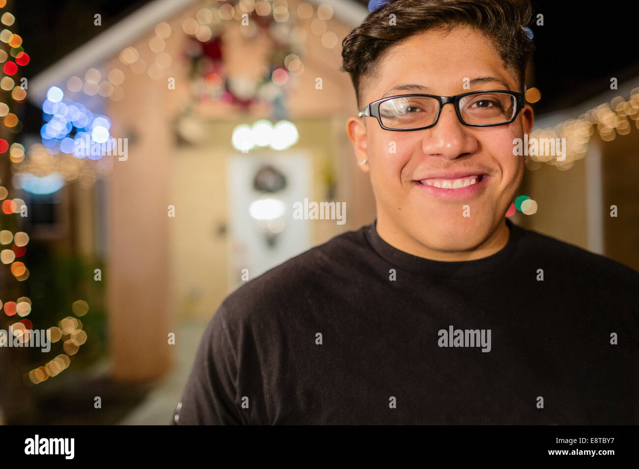 Hispanic man smiling outside house decorated with string lights Stock Photo