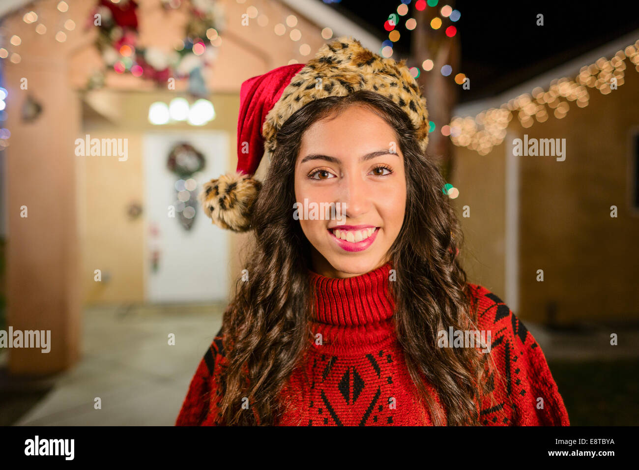 Hispanic woman smiling outside house decorated with string lights Stock Photo
