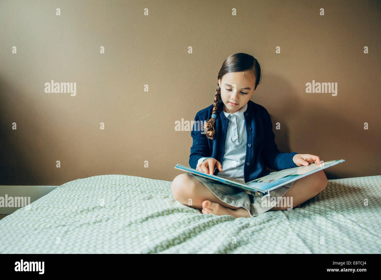 Mixed race girl reading book on bed Stock Photo