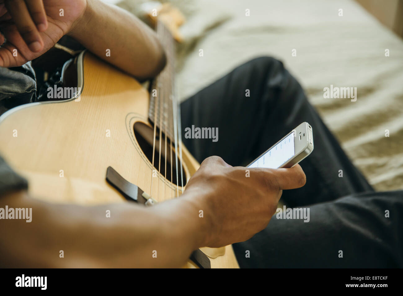 Mixed race boy with guitar using cell phone Stock Photo