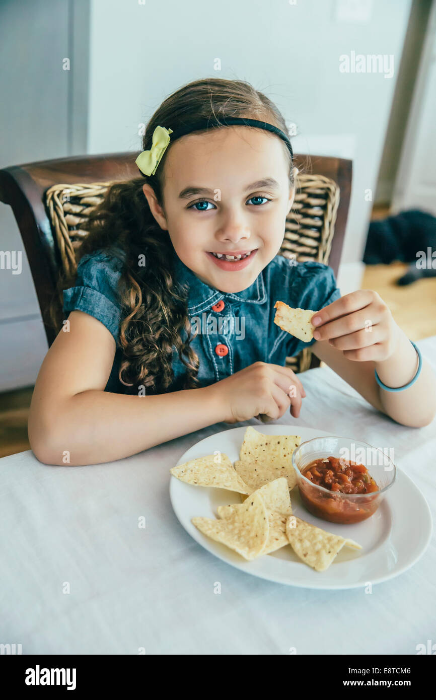 Mixed race girl eating chips and salsa at table Stock Photo Alamy