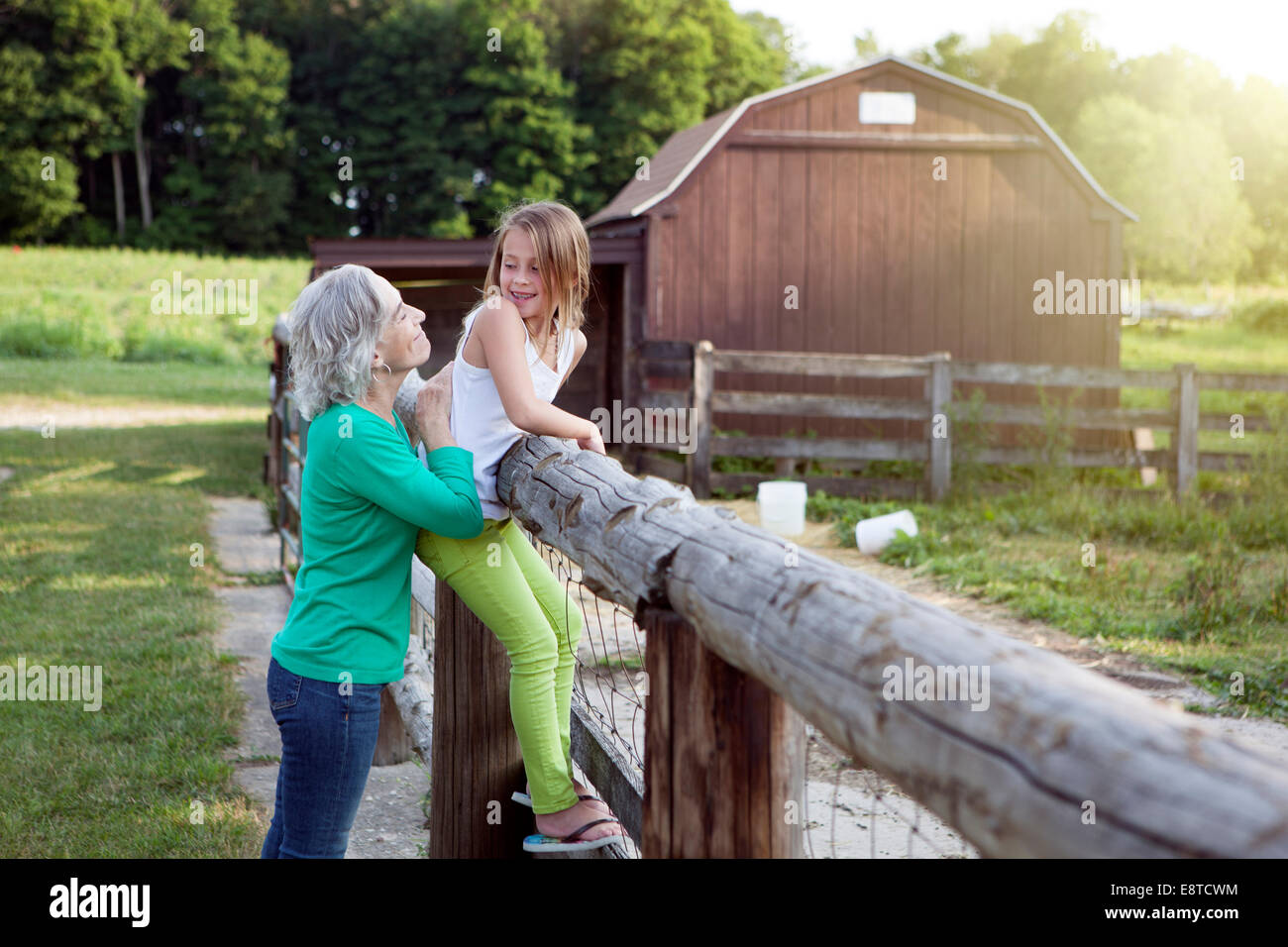 Caucasian grandmother and granddaughter smiling at farm fence Stock Photo