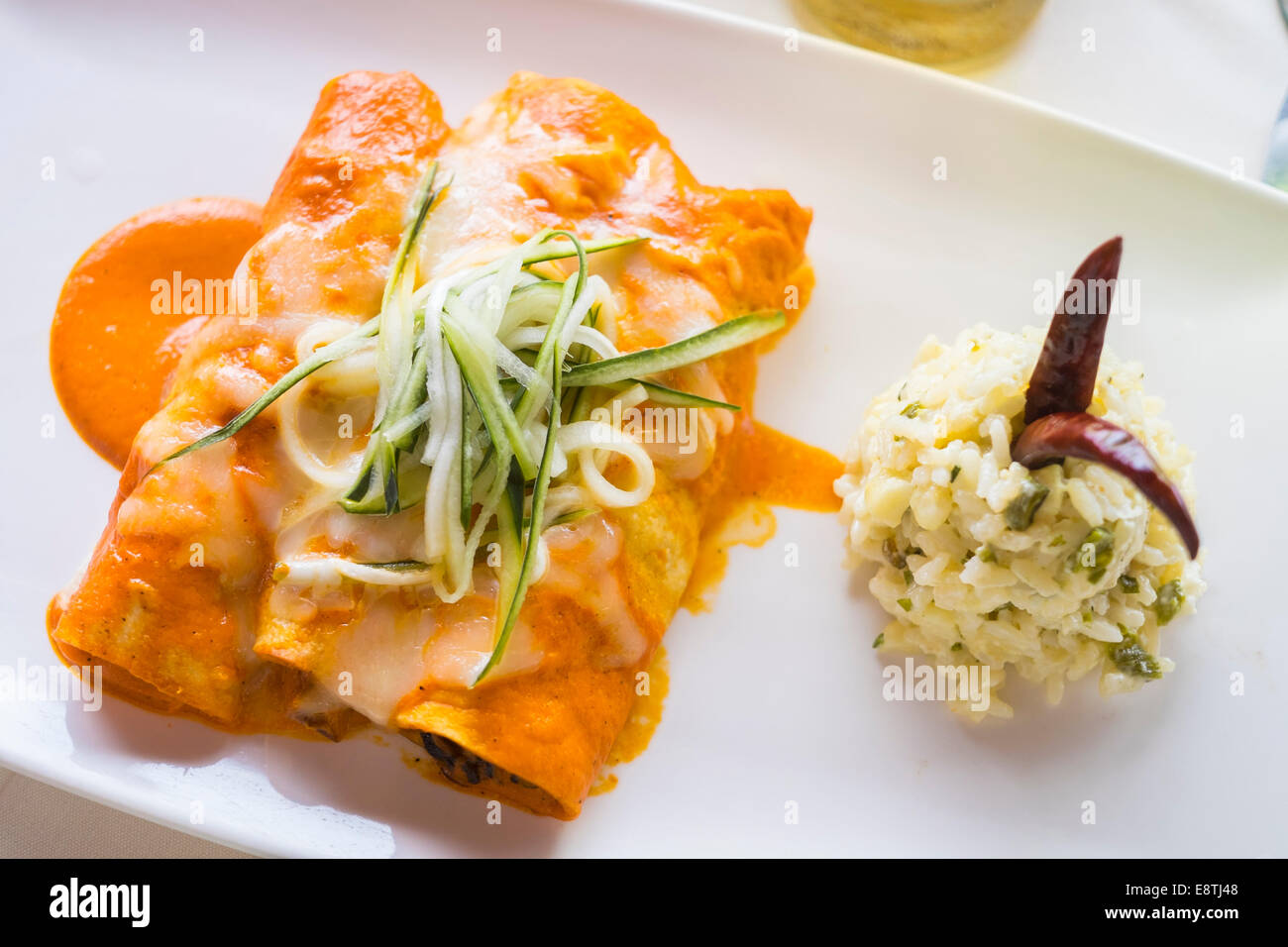 3 enchilada wraps in red pepper sauce, filled with pieces of seafood like oktopus and shrimp. Herbal rice as side dish. Stock Photo