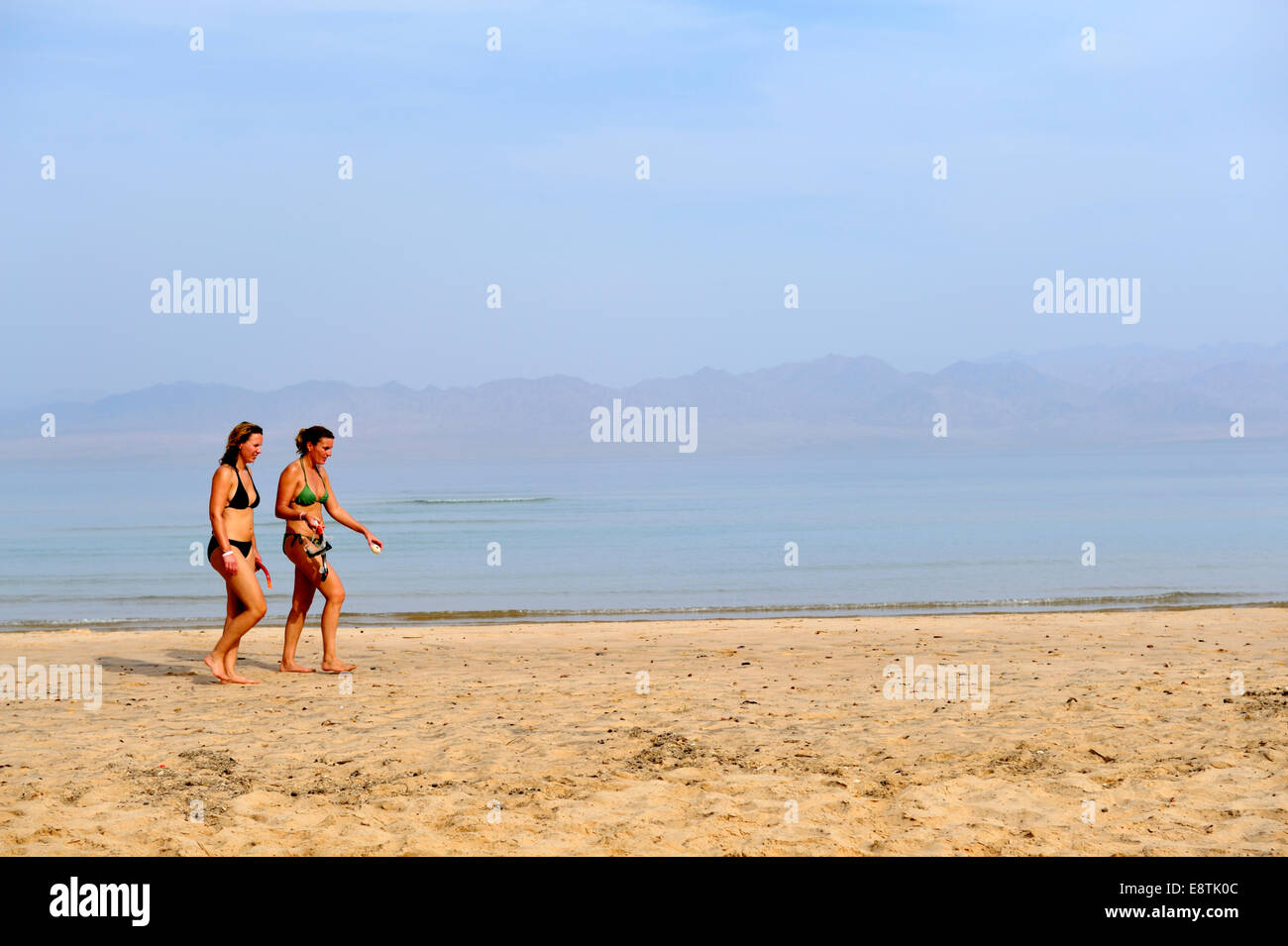 Two women walking along sandy beach at seaside Stock Photo