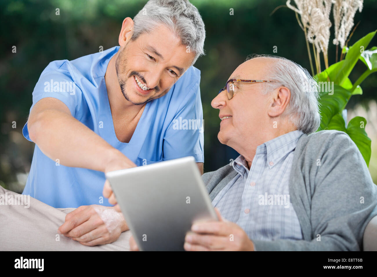 Smiling Nurse Assisting Senior Man Using In Tablet PC Stock Photo