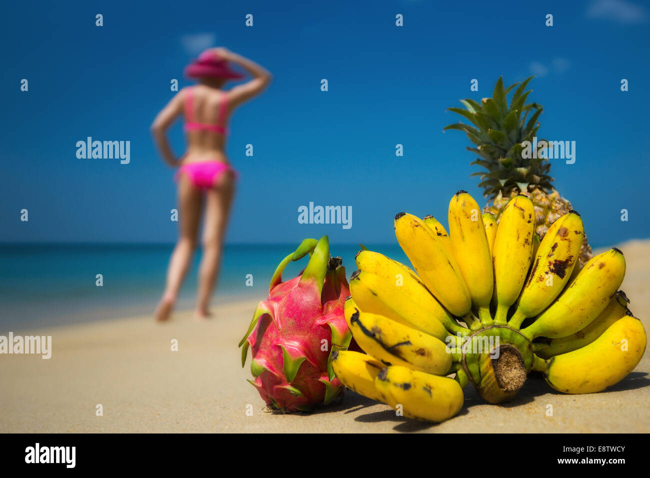 Tropical fruits and a woman in a bikini sunbathing on the beach on sea background. Idealistic scene leisure travel. Stock Photo