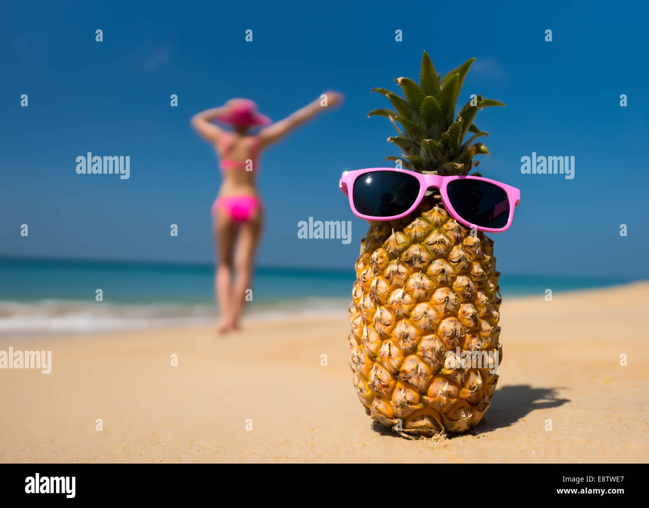 Cheerful pineapple glasses and a woman in a bikini sunbathing on the beach on sea background. Idealistic scene leisure travel. Stock Photo