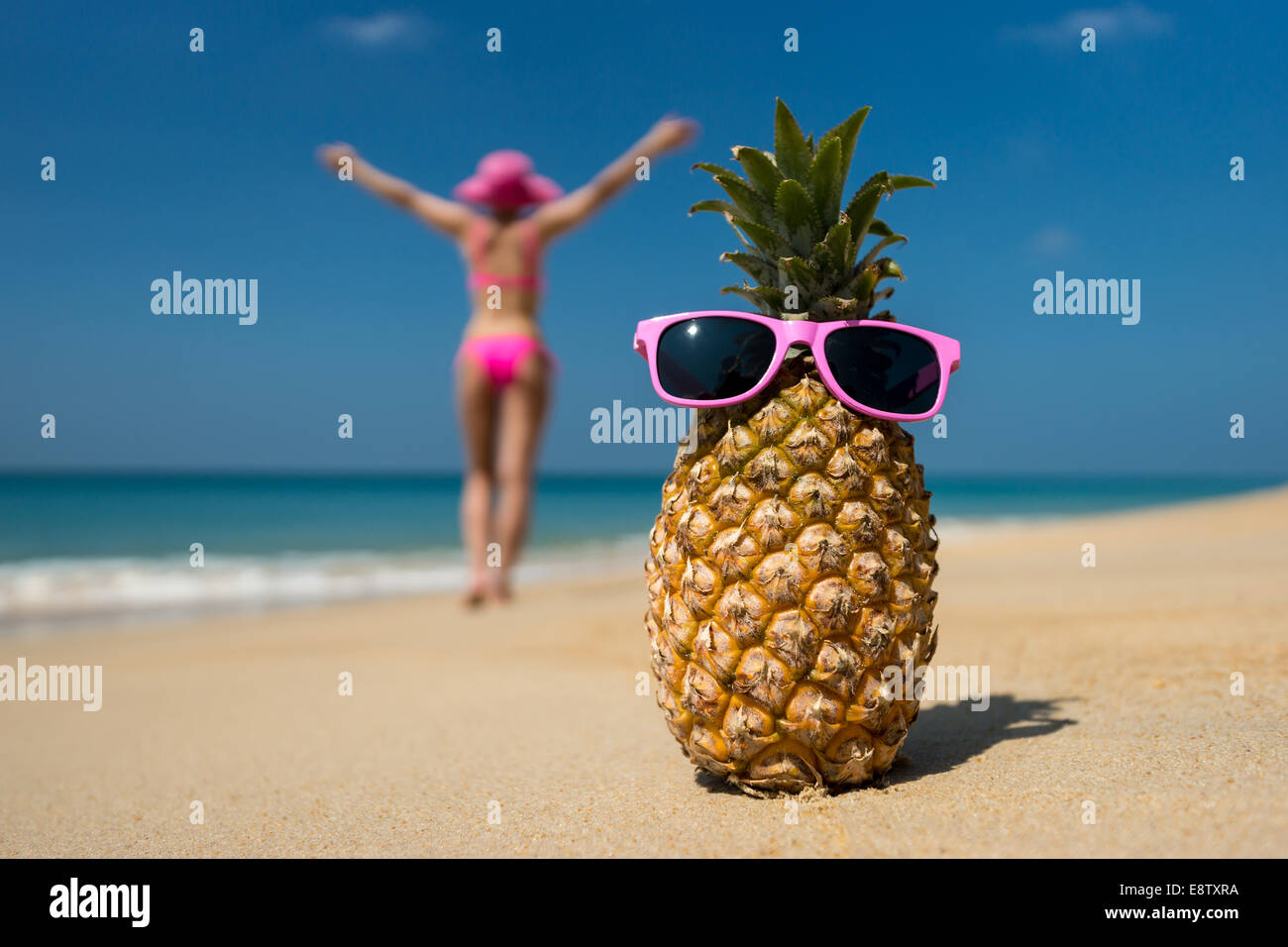 Cheerful pineapple glasses and a woman in a bikini sunbathing on the beach on sea background. Idealistic scene leisure travel. Stock Photo
