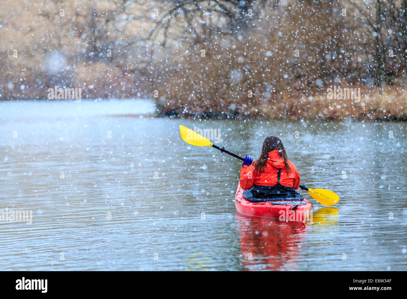 Woman is kayaking on a lake under heavy snow Stock Photo