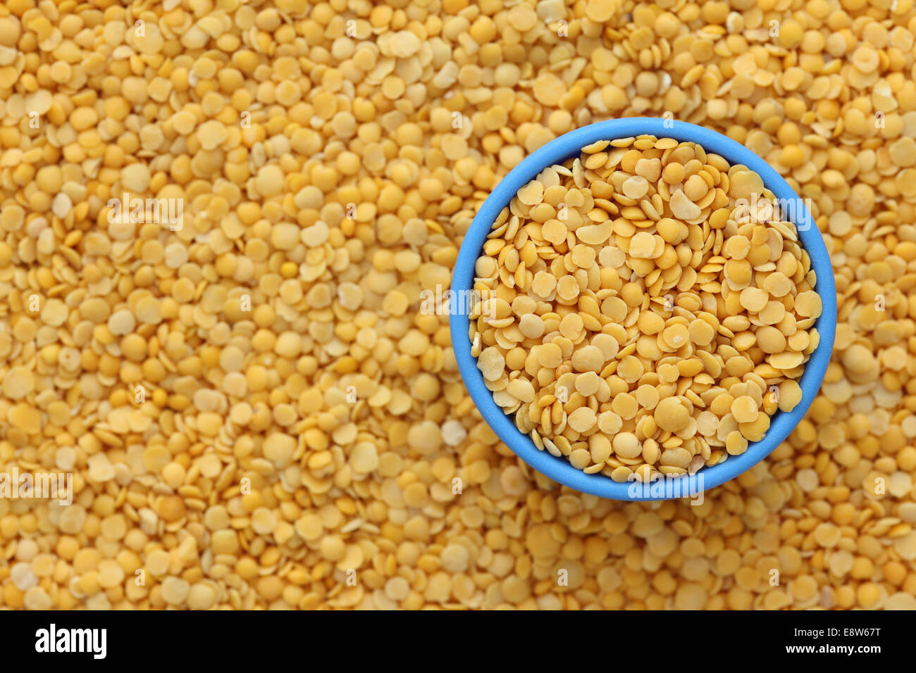 Yellow split lentils in a blue bowl on lentil background. Close-up. Stock Photo