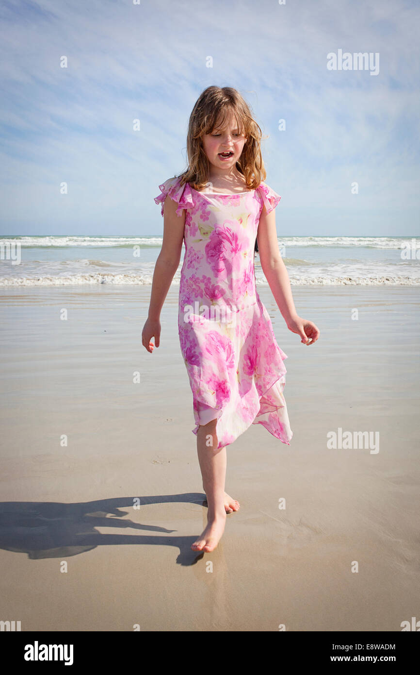 Pretty nine year old girl in a floral pink dress walking along the beach Stock Photo
