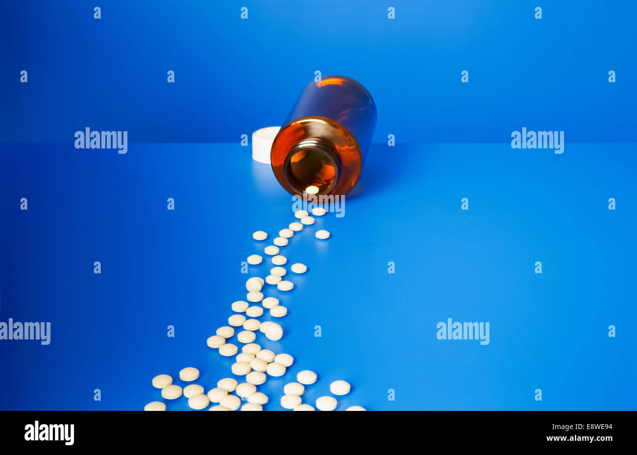 Prescription pills spilling out of bottle onto blue counter Stock Photo