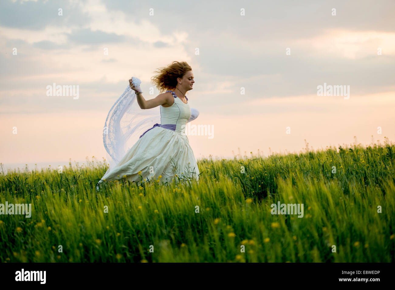 The runaway bride - a young woman girl in a wedding dress running away  fleeing in a field of yellow flowers evening Stock Photo - Alamy