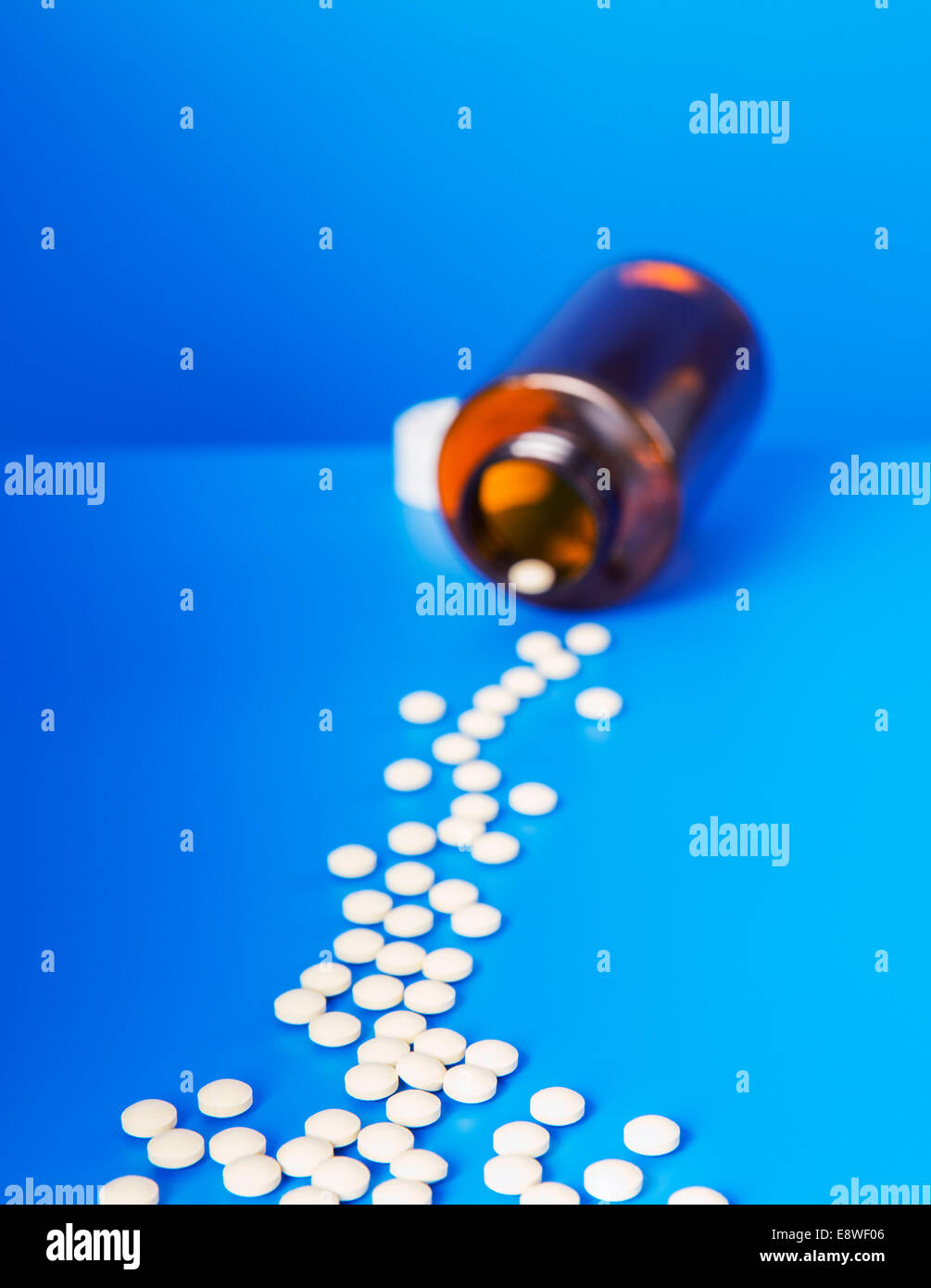 Prescription pills spilling from bottle onto blue counter Stock Photo