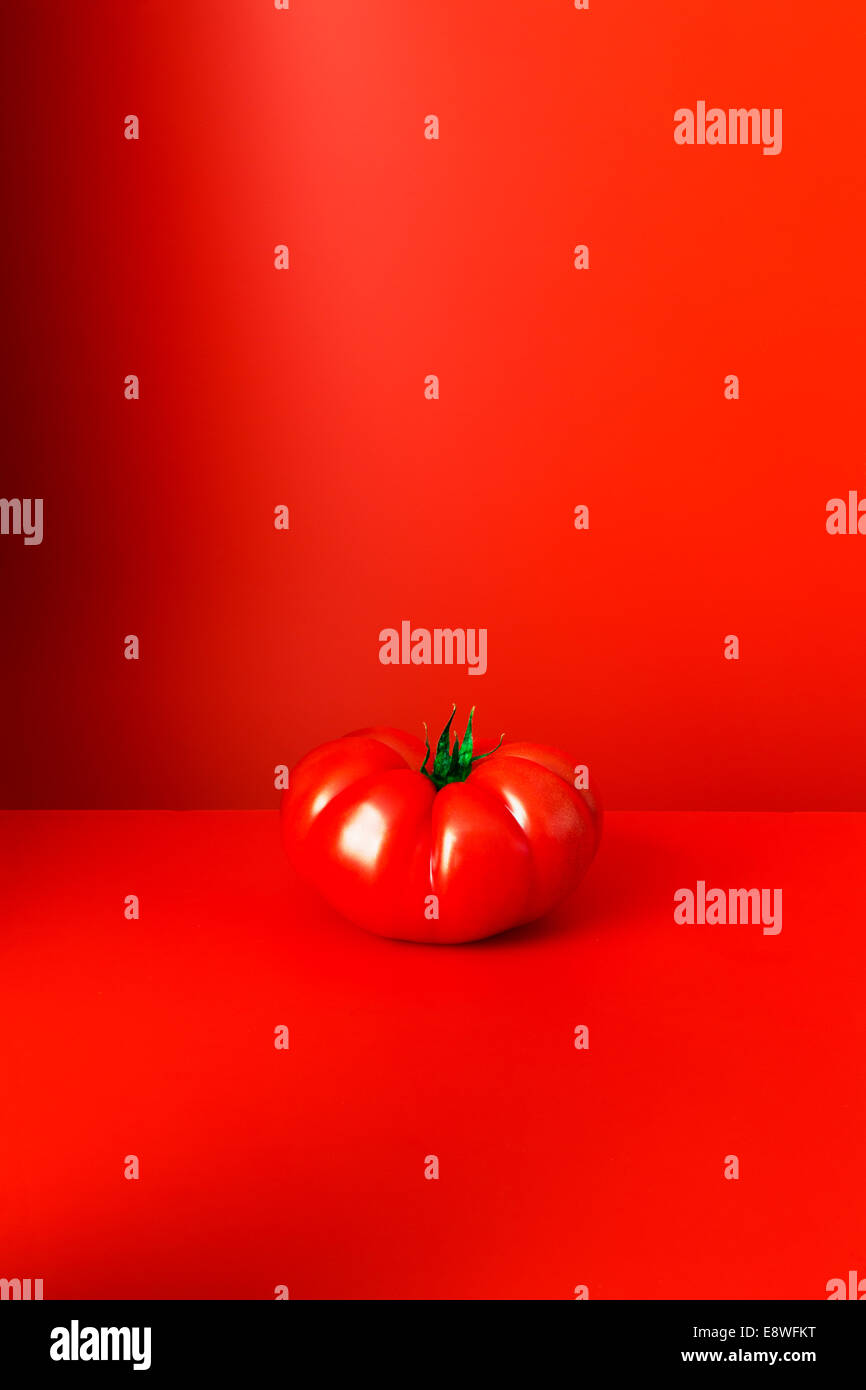 Tomato sitting on red counter Stock Photo