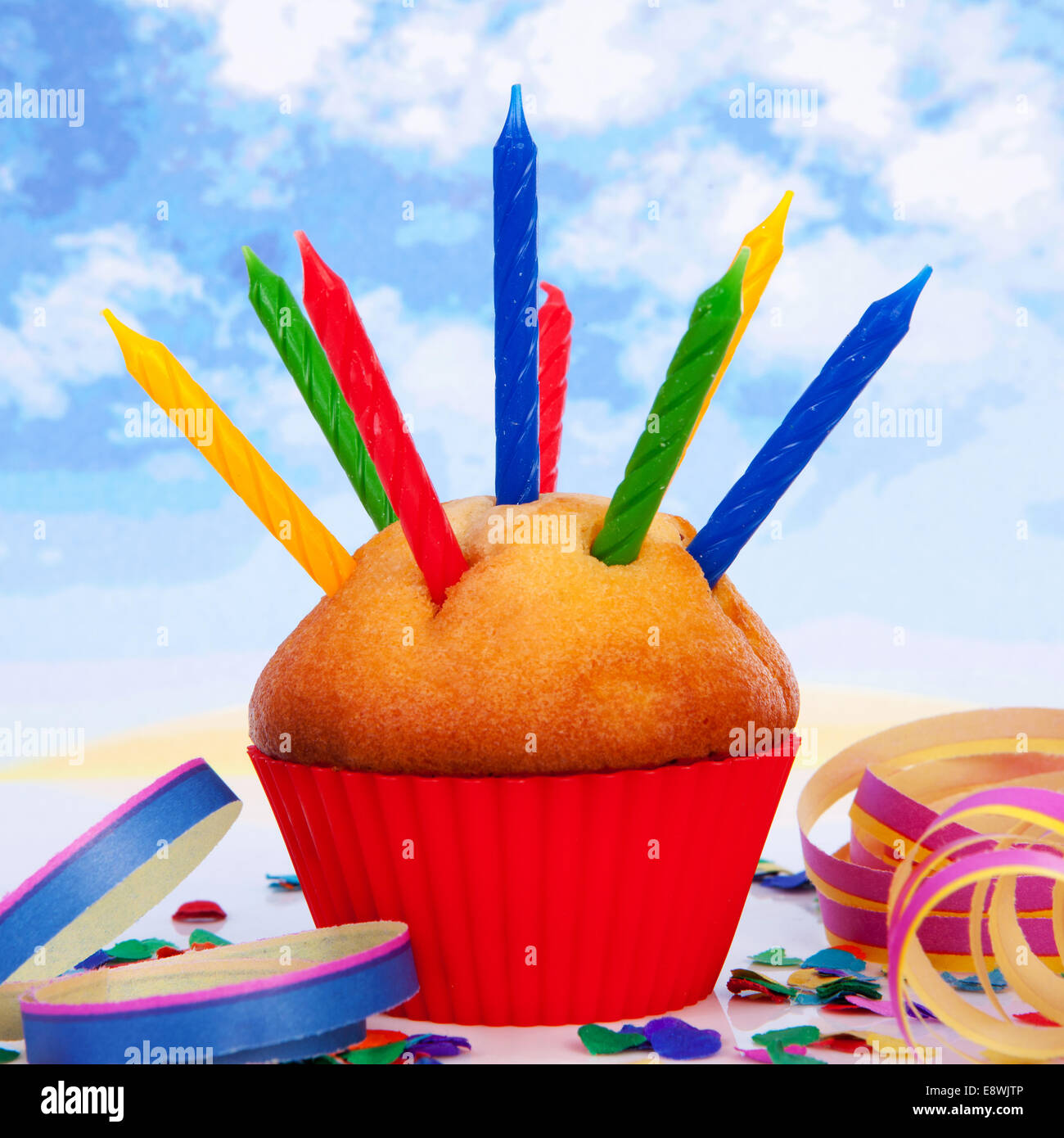 Birthday cupcake with lots of candles and colorful confetti over cloudy