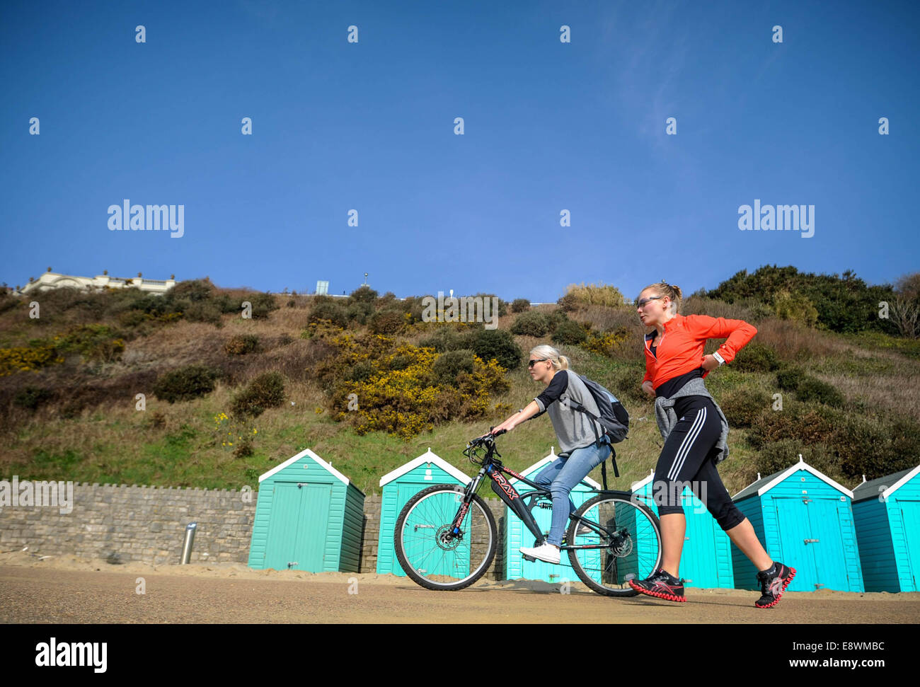 Two women are seen exercising in the sun in front of beach huts on the sea front in Bournemouth Stock Photo