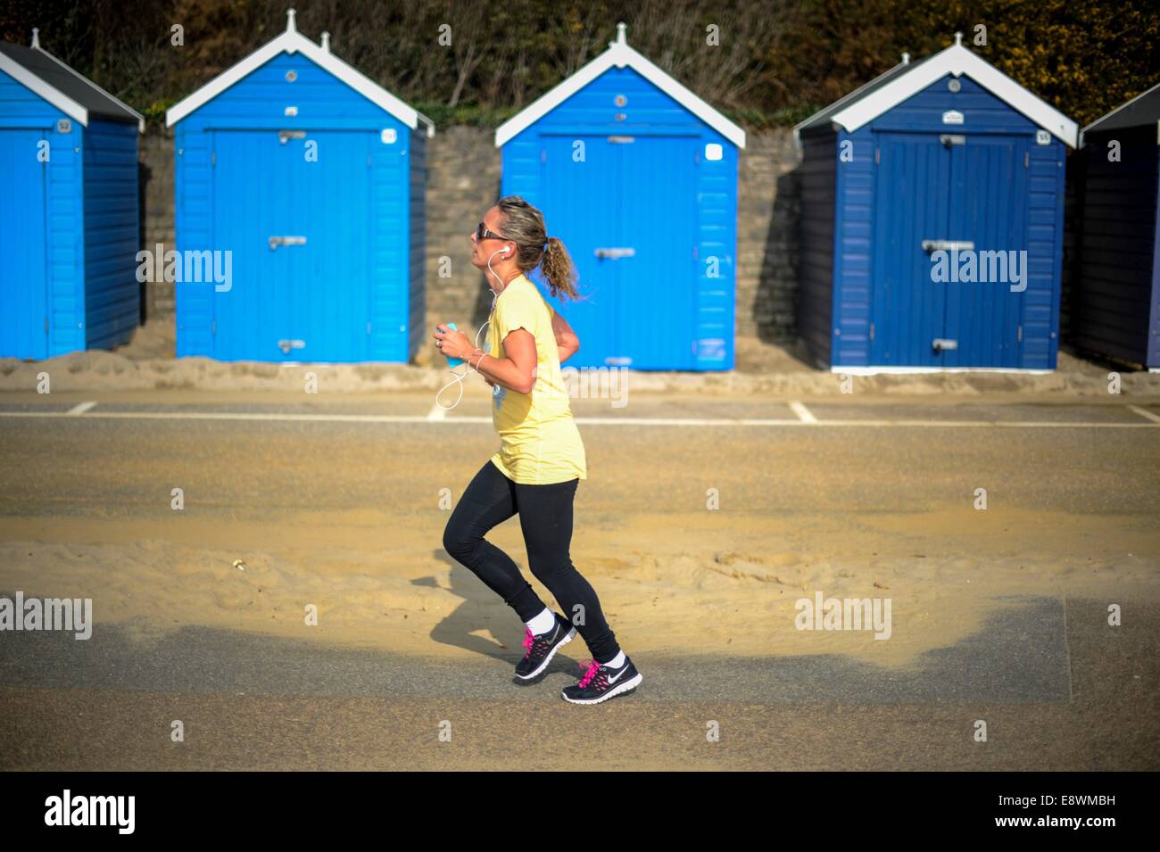 A woman is seen running past a row of beach huts beside the beach in Bournemouth, England Stock Photo
