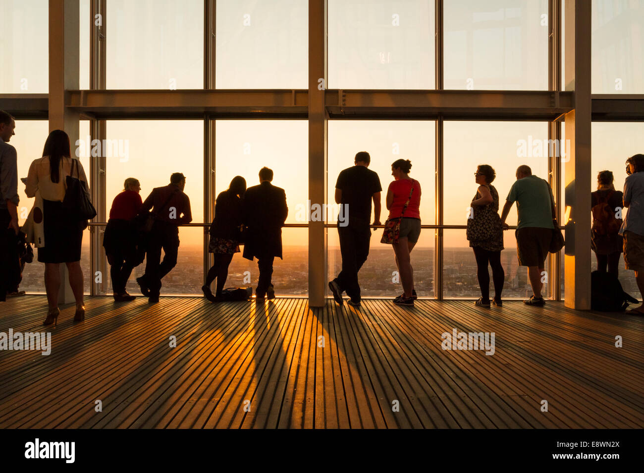 Group of people silhouetted against the the sky and setting sun while viewing London through windows at the top of The Shard, London, England, UK Stock Photo