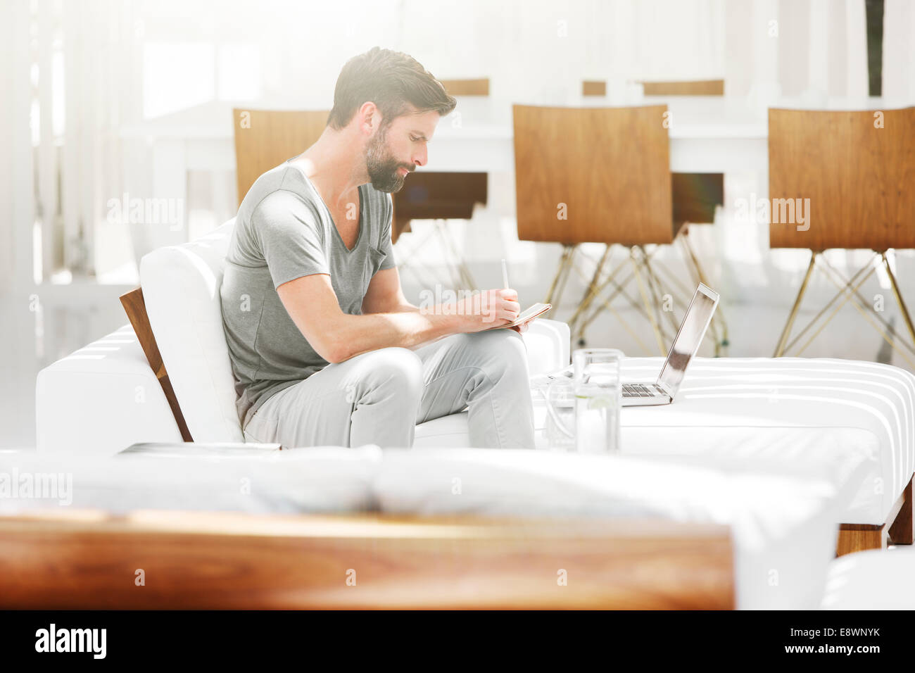 Man writing notes at laptop on sofa in modern living room Stock Photo