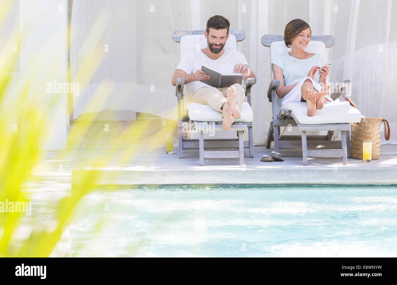 Couple relaxing in lawn chairs by swimming pool Stock Photo
