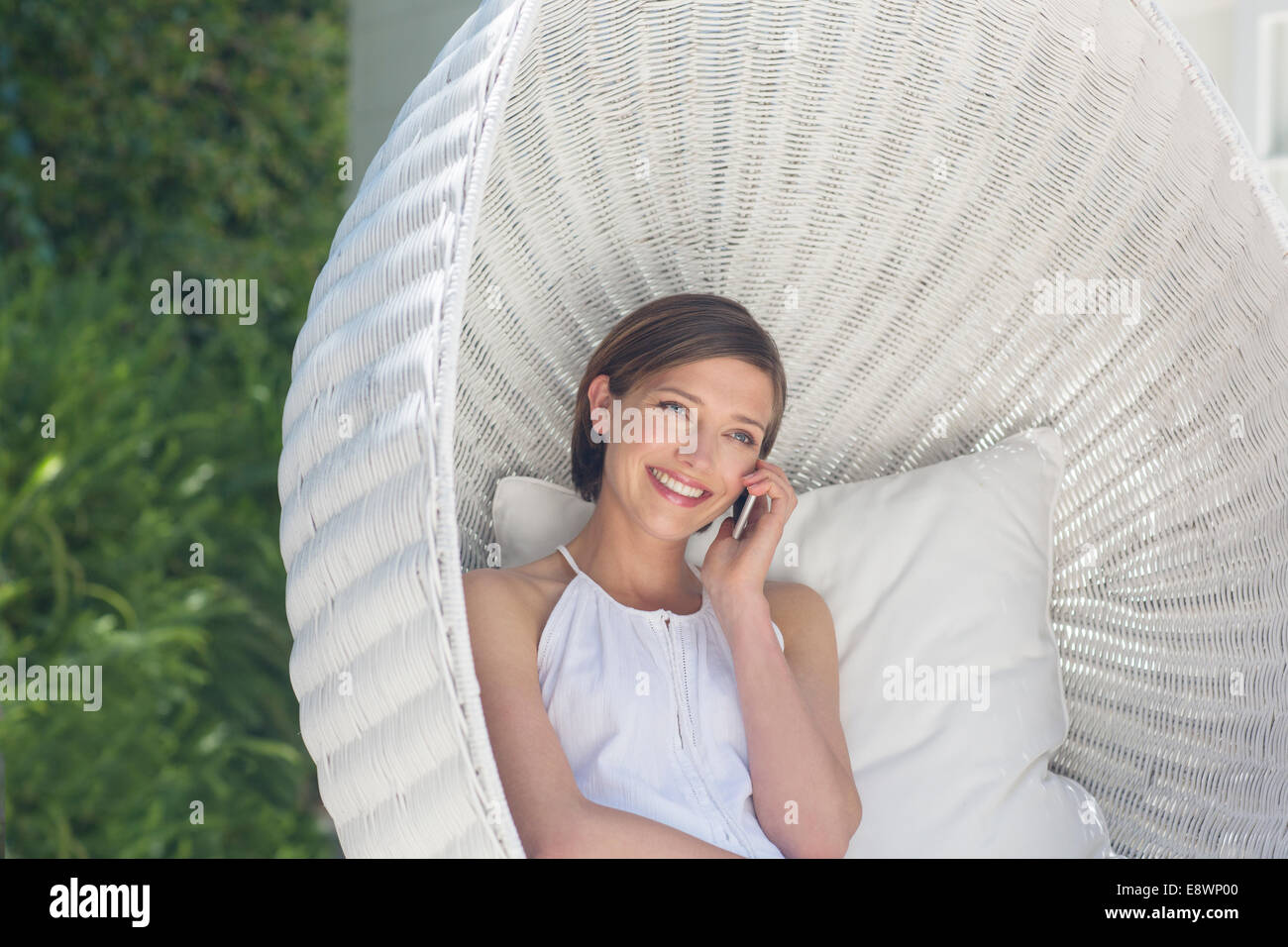 Woman talking on cell phone in hanging wicker chair outdoors Stock Photo