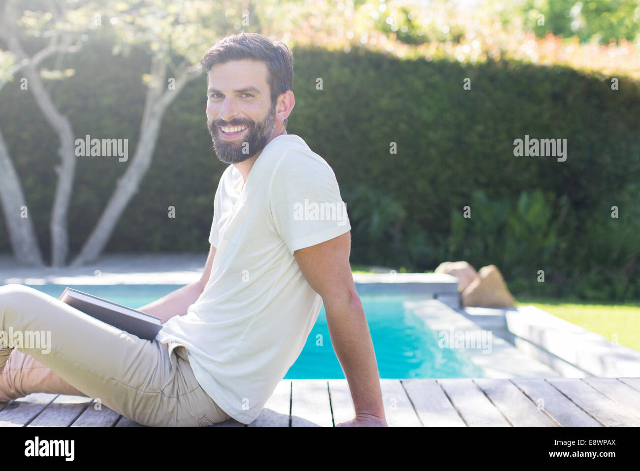 Smiling man relaxing on wooden deck by swimming pool Stock Photo